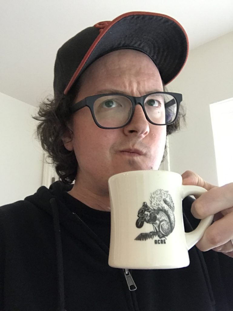 Me wearing black rimmed glasses and a SF Giants hat holding a coffee mug up close to my face with a quizzical look on my face.